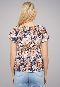 Bloemige peplumtop met korte mouwen, met een marineblauwe achtergrond en veelkleurige bloemen in tinten van oranje, crème en wit.