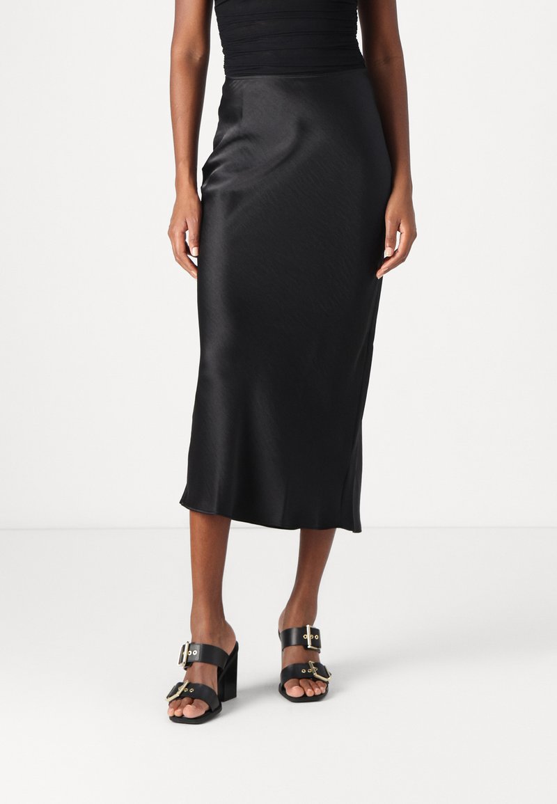 Jupe midi en satin noir avec une texture lisse et un léger éclat. Conception ajustée avec une silhouette droite, associée à des sandales à talons noires.