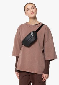 Borsetta in nylon nera con due scomparti con zip, indossata a tracolla sopra un felpa oversize color rosa polveroso.