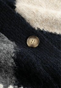 Dzianina swetra o fakturze w kolorach granatowym, kremowym i szarym. Zawiera okrągły, jasny guzik z czterema otworami, ukazujący splecione włókna.