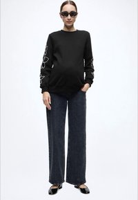 Μαύρο φούτερ με λευκό λουλουδάτο σχέδιο στα μανίκια, συνδυασμένο με σκουρόχρωμο τζιν φαρδιάς γραμμής. Το μοντέλο φοράει μαύρα γυαλιά ηλίου και γυαλιστερές μπαλαρίνες.