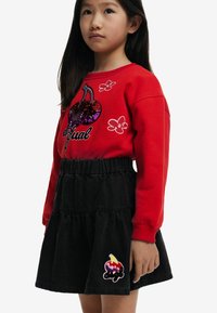Sudadera roja con diseño de cereza de lentejuelas y texto "Igual", combinada con una falda de mezclilla negra con capas que presenta un colorido parche de helado.