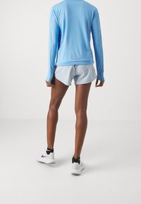 Person som står med ryggen mot kameran iförd en ljusblå långärmad träningströja, ljusblå shorts, svarta strumpor och vita Nike-sneakers.