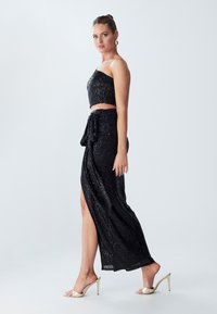 Black sequin two-piece outfit featuring a strapless crop top and a floor-length skirt with a side slit, tied at the waist.