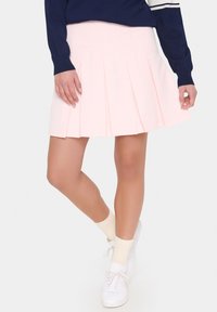 Light pink pleated skirt made of fabric, featuring a flared design. Worn with a navy sweater and white sneakers with cream socks.