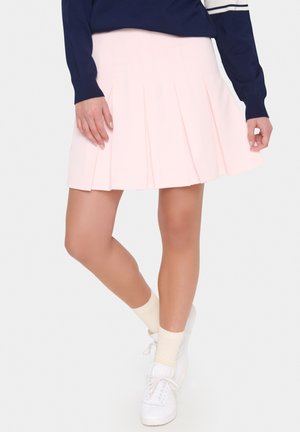 Falda plisada de color rosa claro hecha de tejido, con un diseño acampanado. Se lleva con un suéter azul marino y zapatillas blancas con calcetines de color crema.