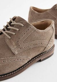 Suède bruin geklede schoenen met perforaties, vetersluiting en een contrasterende zwarte en bruine zool. Glad textuur en ronde neus.