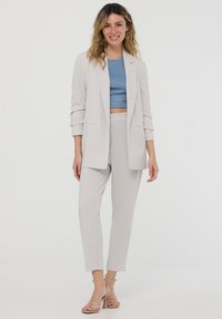 Blazer grigio chiaro su un top corto blu e pantaloni coordinati. Tessuto morbido con vestibilità ampia, accessoriato con tacchi beige con fasce.