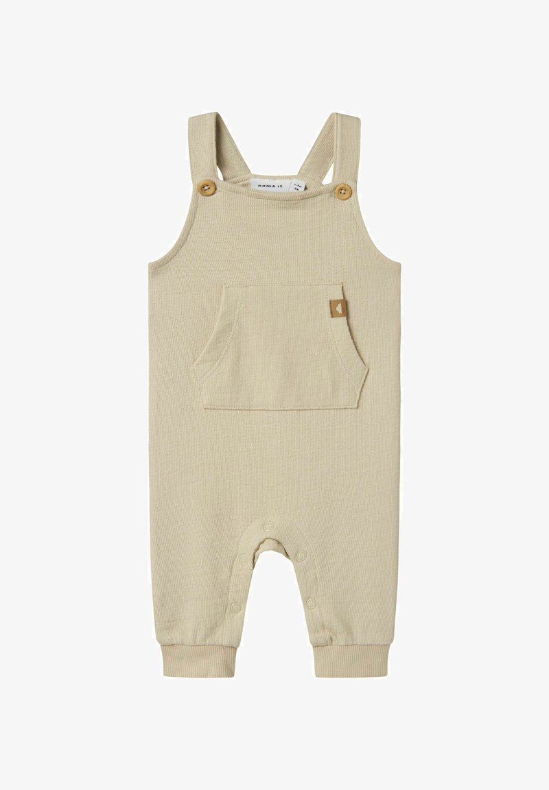 Bodysuit beige à côtes avec bretelles ajustables, boutons en bois, poche frontale et fermetures à pression au bas pour un habillage facile.