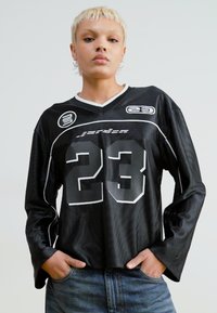 Svart langermet jersey med hvite detaljer, med et stort "23"-nummer og sporty logo detaljer, laget av teksturert meshstoff.