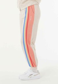 Lichtgrijze joggers met roze en regenbooggestreepte zijpanelen, voorzien van een omslagzoom en een zak, gecombineerd met witte sneakers.