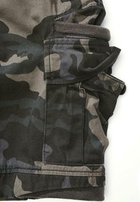 Kamufliažiniai krovininiai šortai, kuriuose dera tamsiai žalia ir pilka spalvos, daugybė kišenių ir minkšta audinio tekstūra.