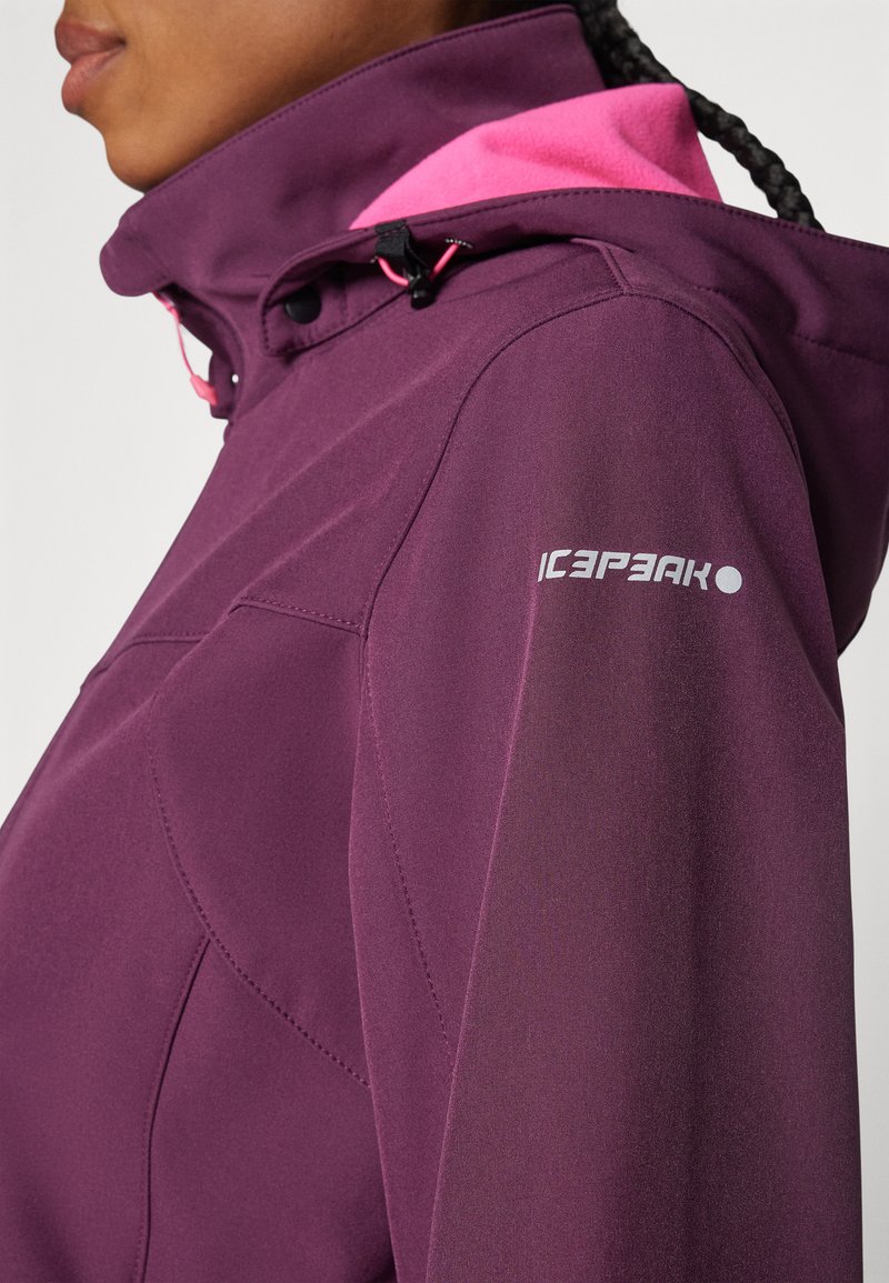 Lila wasserdichte Jacke mit pinken Kapuzenakzenten, ausgestattet mit hohem Kragen, Kordelzugverschluss und Logo am Ärmel. Glatte Textur.