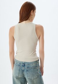 Top sin mangas de canalé en color beige con un diseño ajustado, que presenta un escote redondo, combinado con unos vaqueros de tiro alto en azul claro.