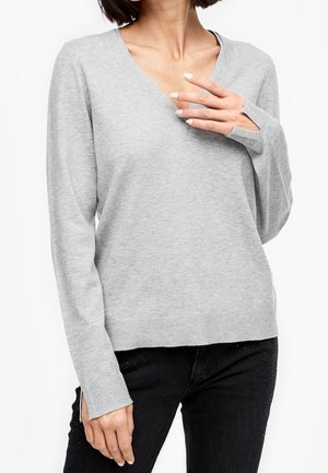 Maglione grigio a V con maniche lunghe, orlo a coste e spacchi laterali; tessuto morbido a maglia, appoggiato su uno sfondo bianco semplice.