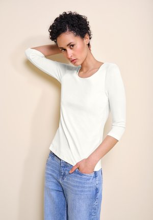 Weißes Langarmshirt mit Rundhalsausschnitt, aus glatter Baumwolle, kombiniert mit hellblauen, lässigen Jeans.