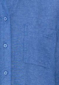 Light blue linen shirt featuring a button front, small chest pocket, and subtle texture. Stitched accents are visible on the pocket edges.
