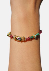 Bracelet doré avec des perles variées en turquoise, ruby et cristal transparent. Comprend des accents décoratifs avec un centre floral.