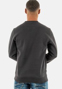 Donkergrijze sweatshirt met een ronde hals, geribbelde manchetten en een gestructureerde afwerking, gecombineerd met blauwe jeans.