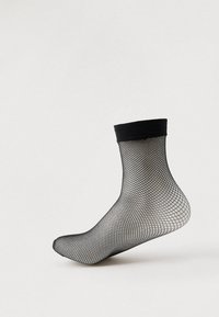 Meia preta de rede exibida num pé de manequim transparente contra um fundo claro simples.