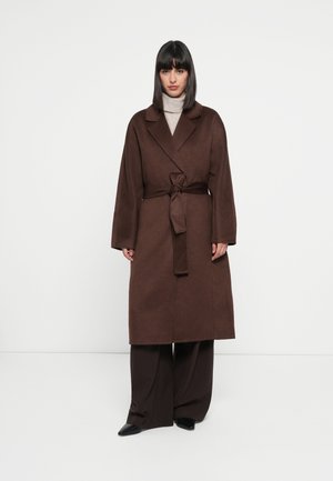 Brown wool blend coat with a wide collar, belted waist, and long sleeves, worn over matching brown wide-leg trousers and black pointed shoes.