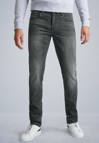 Sive traperice s tapered krojem, s blagim efektom stonewash i klasičnim dizajnom s pet džepova, uparenih s bijelim tenisicama.
