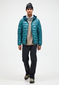 Teal pufferjakke med kviltet mønster, parret med en beige thermotop og sorte vandtætte bukser. Sort hue og grå halsedisse tilføjer tekstur.