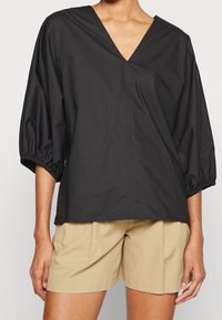 Top nero a scollo a V con maniche a sbuffo tre quarti, caratterizzato da una texture liscia e una vestibilità rilassata, abbinato a pantaloni corti beige.