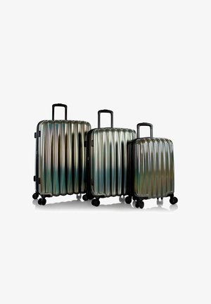 Tre valigie rigide brillanti di diverse dimensioni con motivi a scanalature, dotate di maniglie e ruote nere. Il colore passa dal silver al blu-verde.