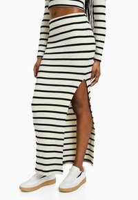 Jupe maxi rayée noir et blanc à côtes avec une fente haute, associée à des baskets blanches avec semelles en gomme et accents noirs.