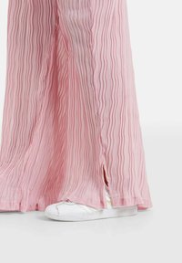 Roze geplisseerde wijde broek met verticale strepen, met zijsplitten. Gecombineerd met witte sneakers, en toont een textuur van de stof.