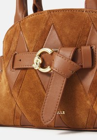 Sac à main en daim et cuir marron avec un motif en losanges, doté d'un fermoir circulaire doré et d'une bandoulière réglable. Nom de la marque en relief.