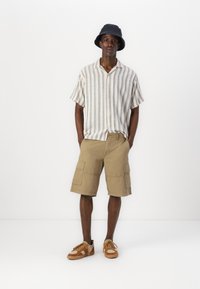 Lettet, stribet T-shirt med korte ærmer i beige og hvid, parret med kaki cargo shorts. Brune sneakers fuldender outfittet.