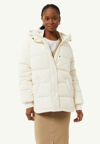 Witte pufferjack met een capuchon, ritsluiting en zijzakken. Gequilt ontwerp met een gladde textuur, gedragen over een geribde beige rok.