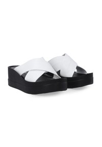 Weiße Sandalen mit Kreuzriemen und dicker schwarzer Plateausohle, die aus glattem Material bestehen und ein schlankes, minimalistisches Design aufweisen.