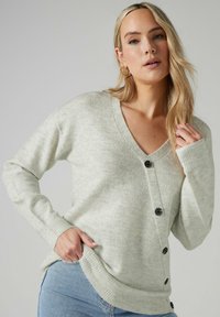 Cardigan lavorato a maglia grigio chiaro con scollo a V, bottoni neri sul davanti e polsini a coste. Tessuto morbido e tasche laterali.
