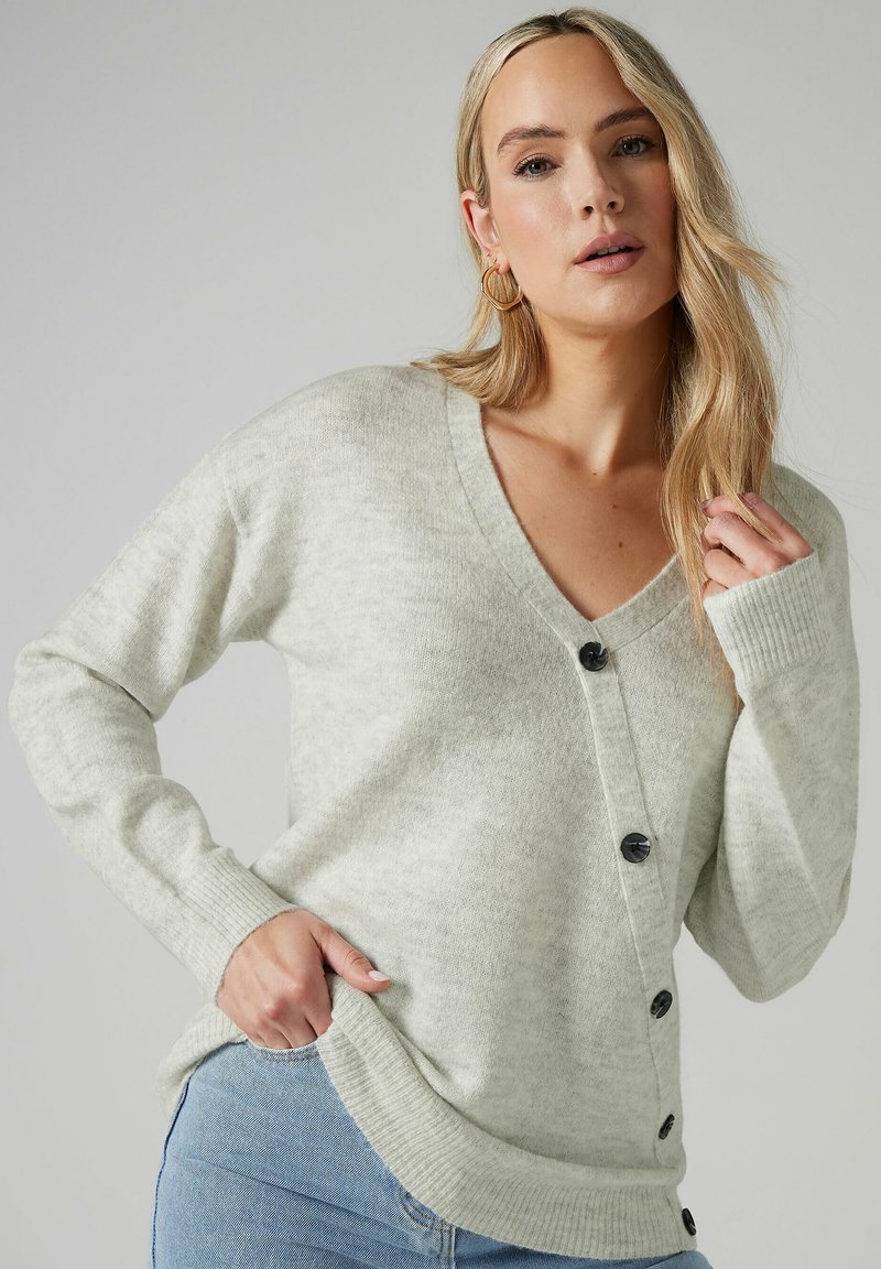 Cardigan lavorato a maglia grigio chiaro con scollo a V, bottoni neri sul davanti e polsini a coste. Tessuto morbido e tasche laterali.