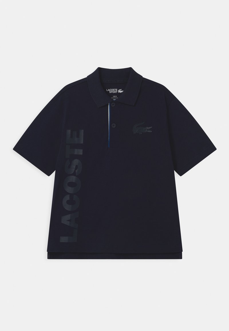 Polo shirt Lacoste Sport blu navy con maniche corte, abbottonatura a due bottoni, grande scritta verticale "LACOSTE" e logo del coccodrillo sul petto.