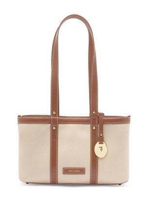 Beżowa prostokątna torba typu tote z brązowymi skórzanymi uchwytami, lamówką, złotym metalowym wykończeniem oraz wiszącym okrągłym złotym ozdobnikiem.