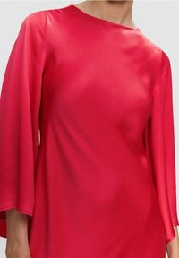 Blouse rouge en soie avec un col bateau et des manches larges et amples. Texture lisse avec un léger éclat. Aucun motif visible ni détail matériel.