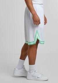 Shorts de sport blancs avec des accents verts, ornés d'un motif contrasté au niveau de l'ourlet et d'une taille élastique. Associés à des baskets blanches.