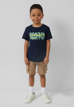 Granatowa bawełniana koszulka z grafiką "TOKYO", beżowe szorty cargo, białe sneakersy i prążkowane białe skarpetki do kostek. Prosty design, swobodny krój.
