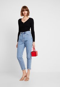 Zwarte geribbelde lange mouw top met een ritssluiting, lichtblauwe hoge taille jeans, beige enkelband sandalen en een kleine rode handtas.