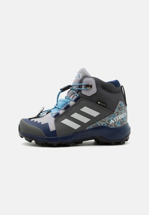 Wysokie szaro-niebieskie buty trekkingowe z czarną podeszwą, jasnoniebieskimi sznurówkami, białymi paskami, etykietą Gore-Tex i cyfrowym kamuflażowym wzorem na pięcie.