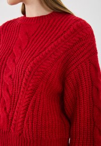 Roter Strickpullover mit Ripp- und Zopfmuster, Rundhalsausschnitt und strukturierter, grober Optik.