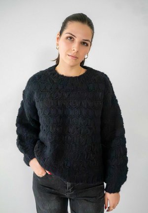Zwarte gebreide trui met een textuurpatroon, ronde halslijn en een losse pasvorm. Gekocht met donkere spijkerbroeken, die een gladde, zachte textuur hebben.