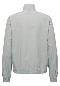 Chaqueta ligera de color gris claro con un collar alto, puños elásticos y dobladillo. Textura suave y diseño minimalista, sin cierres visibles.