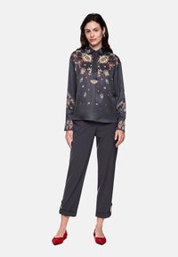 Black patterned blouse with multicolored floral designs, long sleeves, and a collar, paired with dark gray trousers and red flats.