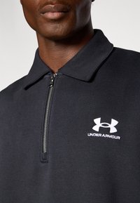 Čierna mikina na zips z mäkkého materiálu s golierom. Na hrudi sa nachádza biele logo Under Armour. Textúrovaný povrch s hladkým dokončením.