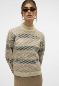 Beige gebreide trui met donkerblauwe geometrische patronen, geribbelde kraag en manchetten, oversized pasvorm, zachte textuur, minimalistisch design.
